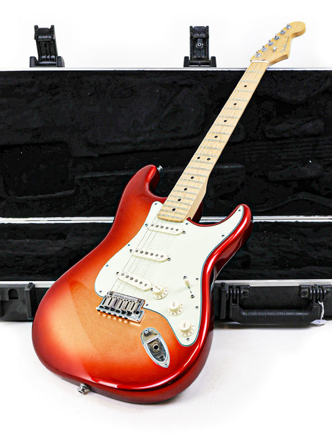 Red and white electric guitar with a maple neck, resting on a black case.
