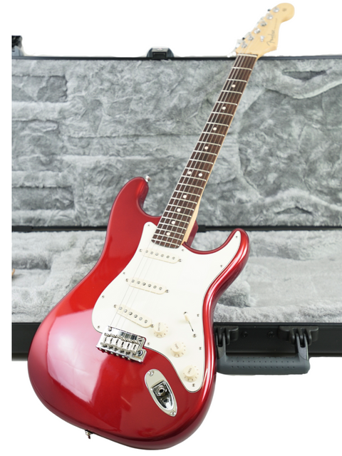 Red electric guitar leaning against a stone wall with a guitar case in the foreground.