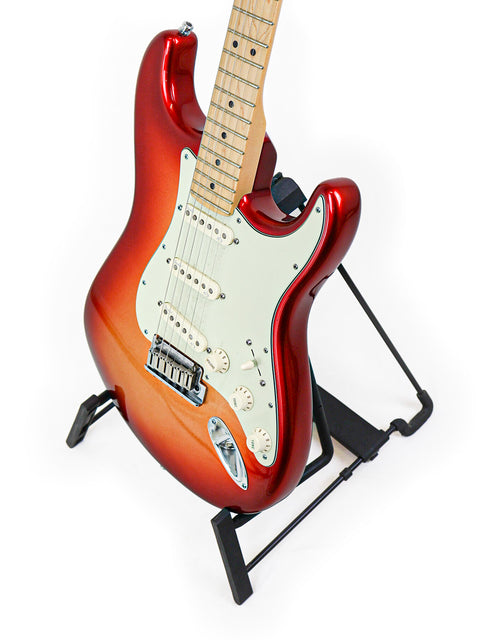 Red electric guitar with a maple neck on a black stand against a white background.