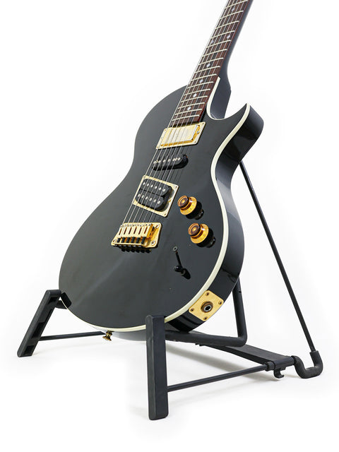 Stunning black Gibson Nighthawk guitar from 1999 on a stand, set against a bright white backdrop. Ideal for collectors and players.