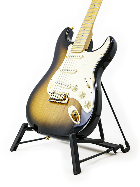 Sunburst electric guitar on a black stand against a white background.