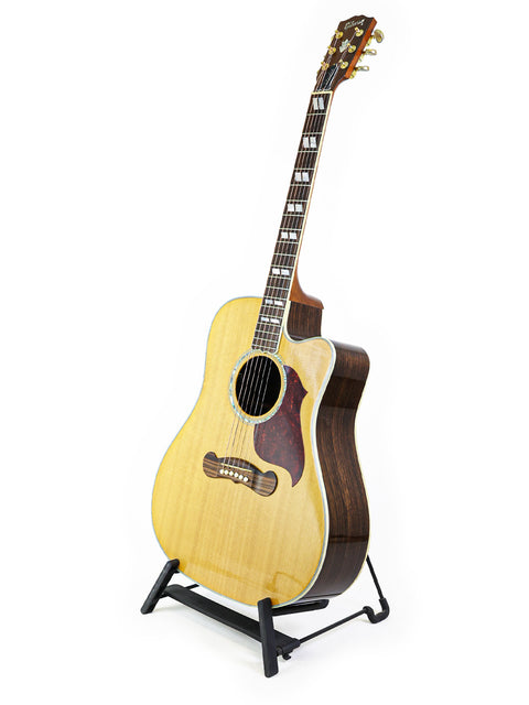 The image features a Gibson Songwriter Studio Deluxe EC -USA 2014 acoustic guitar positioned on a stand.
