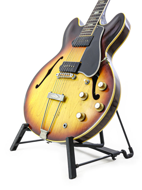 Vintage Gibson ES-330TD guitar from 1964 on a stand, beautifully contrasted by a smooth white background.