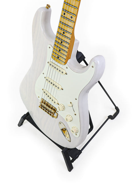 White electric guitar with a maple neck on a black stand, isolated on a white background.