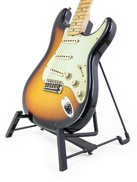 vintage Fender John Cruz Master Built ‘64 Stratocaster Relic guitar displayed on a stand with a dark backdrop.
