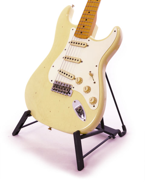 A white guitar, the Fender Ltd Custom 50s Journeyman Stratocaster, elegantly positioned on a black stand.
