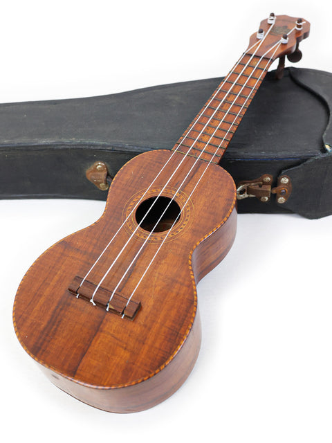 A 1927 Paul F. Summers 'Moana' Style 5 Koa Ukulele and its case, showcased on a plain white surface.