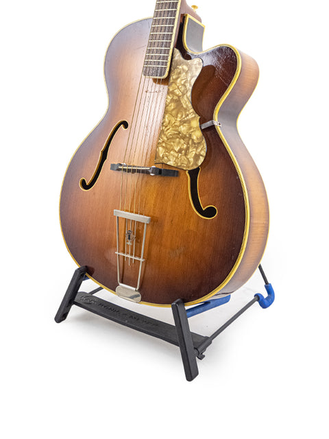 A 1950s Hofner 455 Archtop guitar on a black stand, emphasizing its vintage charm and German craftsmanship.