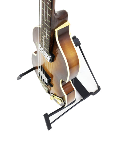 A 1962 Hofner 500/1 'Beatle Bass' guitar displayed on a stand, featuring a strap, highlighting its classic style.