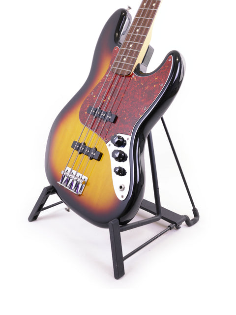 A 2013 Fender Jazz Bass guitar on a stand, contrasted against a bright white background, highlighting its classic design.
