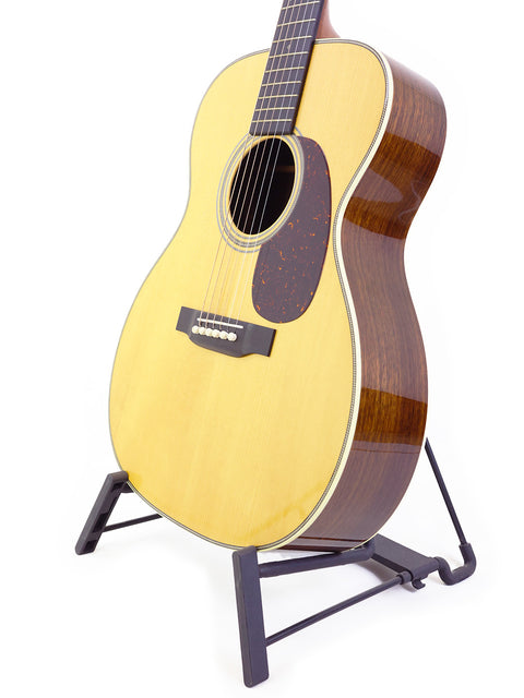 A Martin Custom Shop 000-28 guitar displayed on a stand, featuring a pristine white background that highlights its craftsmanship.
