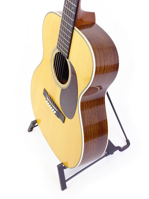 A Martin Custom Shop 000-28 guitar elegantly positioned on a stand, with a simple white backdrop highlighting its craftsmanship.