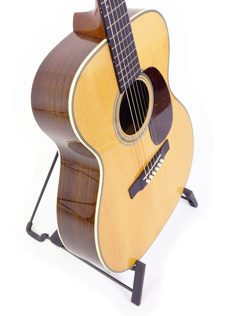 A Martin Custom Shop 000-28 guitar resting on a stand, contrasted against a white background, showcasing its fine details.