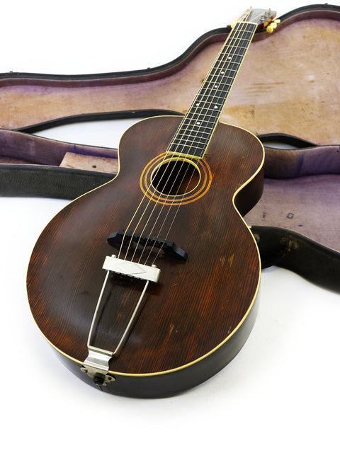 A brown acoustic guitar, a vintage 1920 Gibson L-1, lying in its case on the floor, representing classic musical heritage.