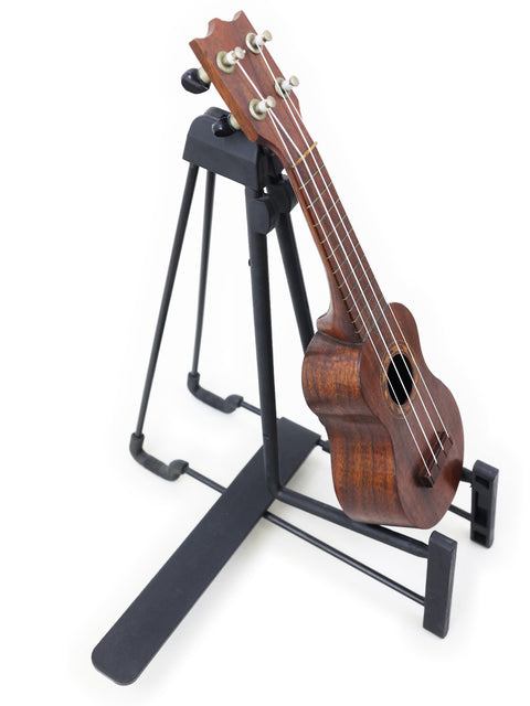 A classic 1917 TABU Style 2 "Midget" Koa Ukulele displayed on a black stand, highlighting its unique Hawaiian craftsmanship.
