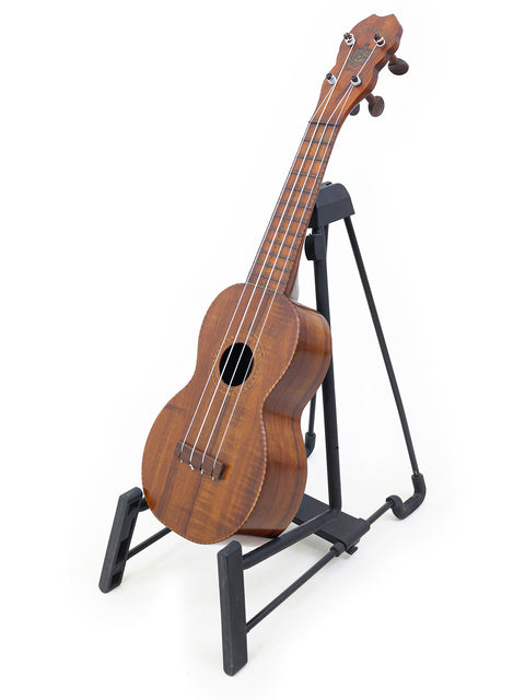 A classic 1927 Paul F. Summers 'Moana' Style 5 Koa Ukulele displayed on a black stand, highlighting its unique features.