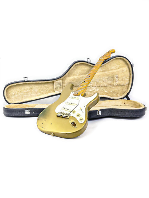 A gold '57 Fender Custom Shop Stratocaster guitar and case resting on a white surface, showcasing its limited edition design.