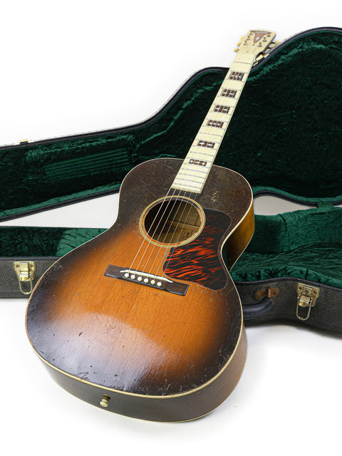 A green case holds a Gibson L-C guitar, a classic piece from the 1936 Century of Progress collection.
