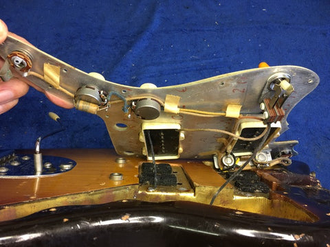 A person grips a vintage Fender Jazzmaster guitar from 1960, revealing its wires and mechanical parts.
