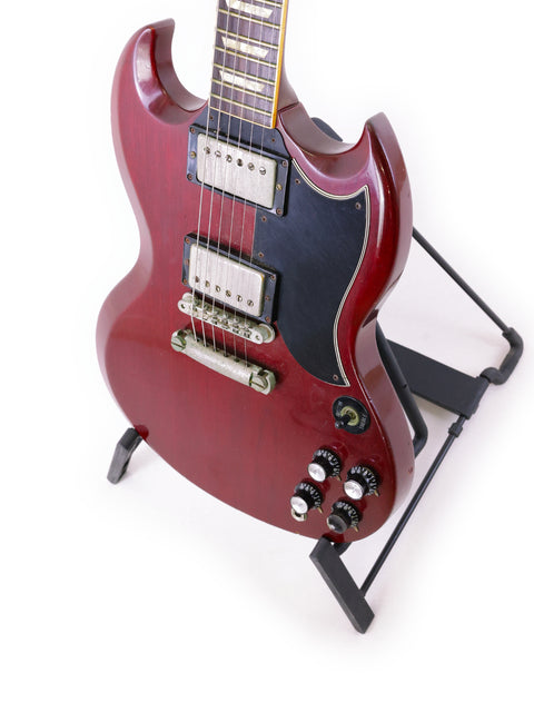 A red 1988 Gibson SG '61 Reissue guitar is displayed on a stand, accompanied by a black guitar strap.