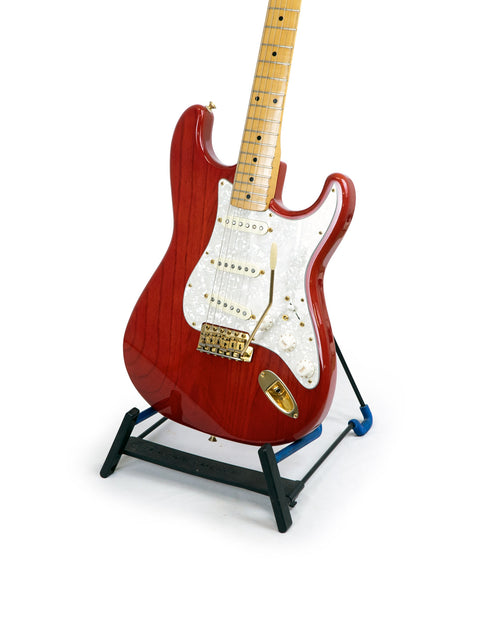 A red Fender MIJ '57 Style Stratocaster guitar elegantly positioned on a stand, with a bright white background enhancing its features.