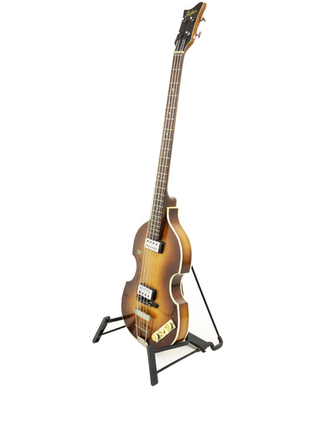 A small Hofner 500/1 'Beatle Bass' guitar elegantly positioned on a stand, contrasted against a bright white backdrop.