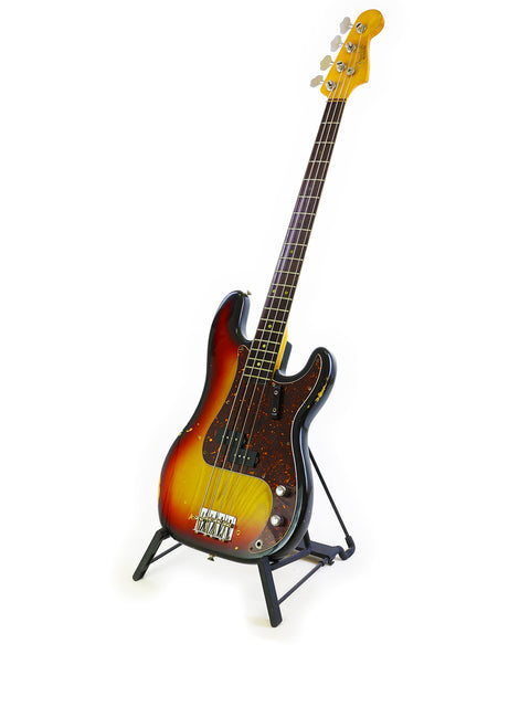 A small electric guitar displayed on a stand, featuring a vintage 1972 Fender Precision Bass with a '63 neck.