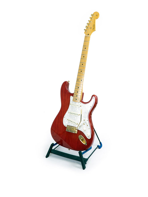 A striking red Fender MIJ '57 Style Stratocaster guitar displayed on a stand, set against a simple white backdrop.
