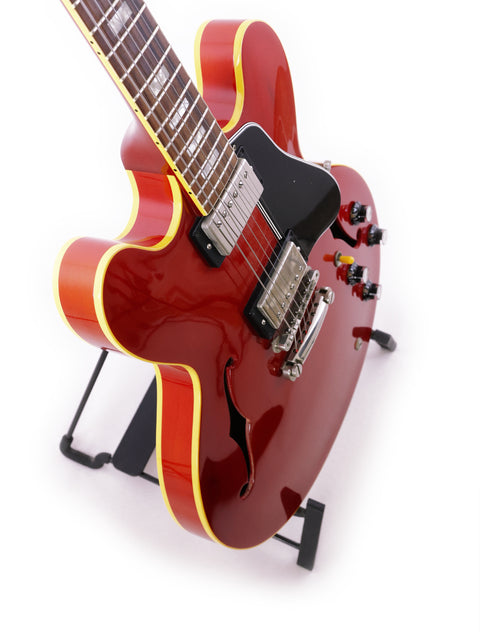 A vibrant red Gibson ES-335 Block guitar, crafted in 1963, sits on a stand, emphasizing its iconic shape and rich history.