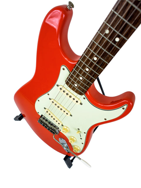 A vibrant red electric guitar, the Fender American Vintage 62 Strat, displayed on a stand with a white backdrop.
