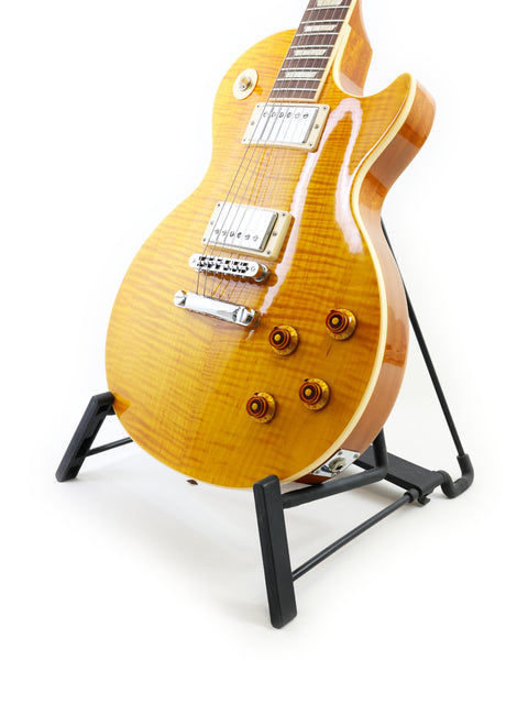 A vibrant yellow Gibson Les Paul Standard guitar is displayed on a sturdy stand, highlighting its classic shape and craftsmanship.