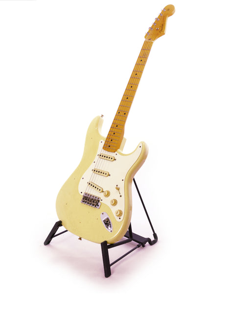 A white guitar, the Fender Ltd Custom 50s Journeyman Stratocaster, rests on a stand featuring a black base.
