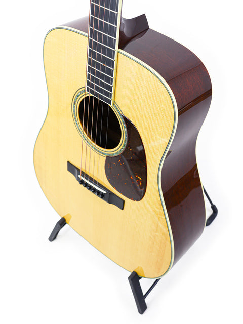Acoustic guitar displayed upright on a stand, isolated against a white background.
