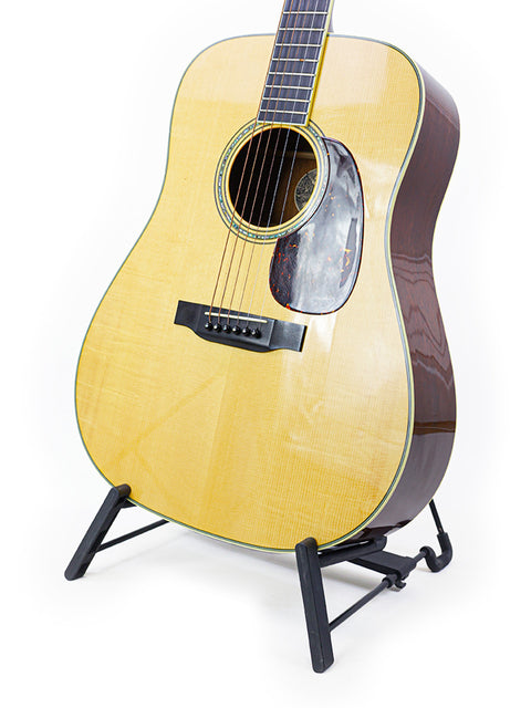 Acoustic guitar on a stand, with a natural finish and dark fretboard, isolated on a white background.