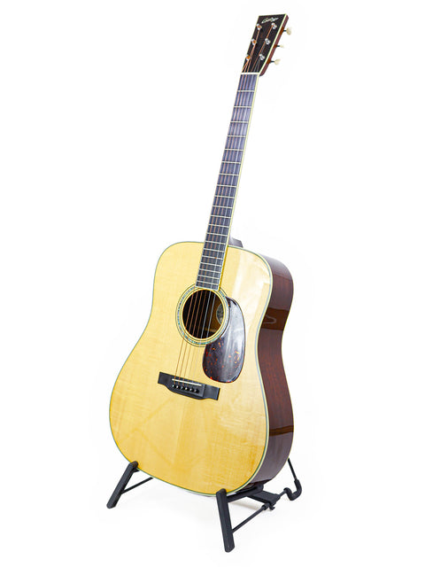 Acoustic guitar on stand against white background.