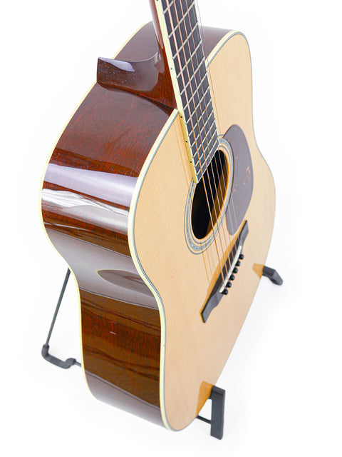 Acoustic guitar standing on floor stand against a white background.