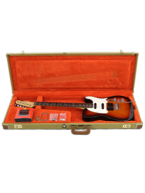 An orange case holds a Fender Telecaster Plus Deluxe guitar from 1992, with a guitar pick resting beside it, ready to play.