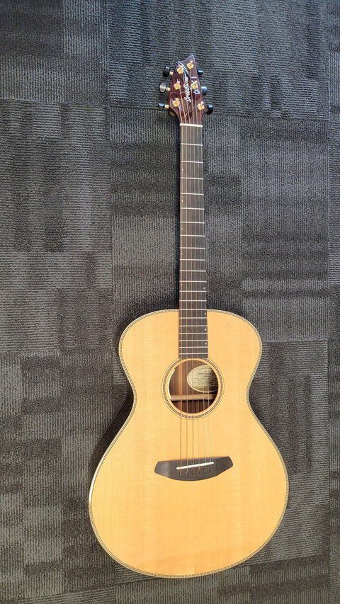 Breedlove Journey Concert guitar rests on the floor against a sleek black background, showcasing its elegant design.
