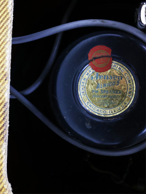 Detailed view of a record player showcasing a striking red label, accompanied by a vintage Fender Tweed Deluxe Amp 5D3 from 1955.