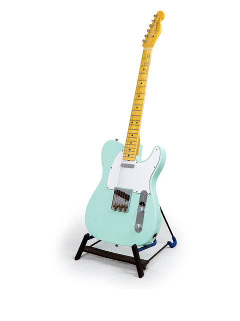 Fender Custom Shop 60s Journeyman Telecaster in green, elegantly positioned on a stand with a white backdrop.
