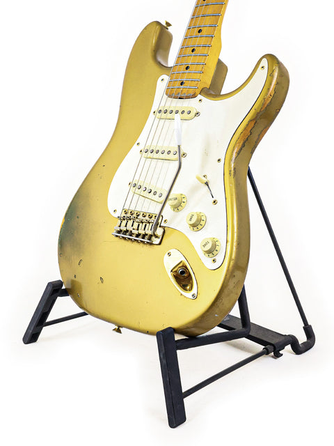 Golden '57 Fender Custom Shop Stratocaster guitar on a stand, showcased with a pristine white background.