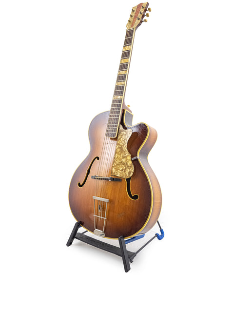 Hofner 455 Archtop guitar from the 1950s on a stand, set against a white background, emphasizing its vintage charm.