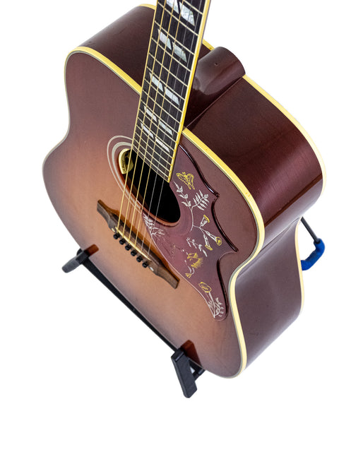 Inside a pink guitar case lies a Gibson Hummingbird True Vintage guitar, highlighting its classic beauty and craftsmanship.