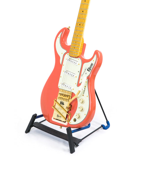 Red electric guitar with a maple neck on a black stand, isolated on a white background.