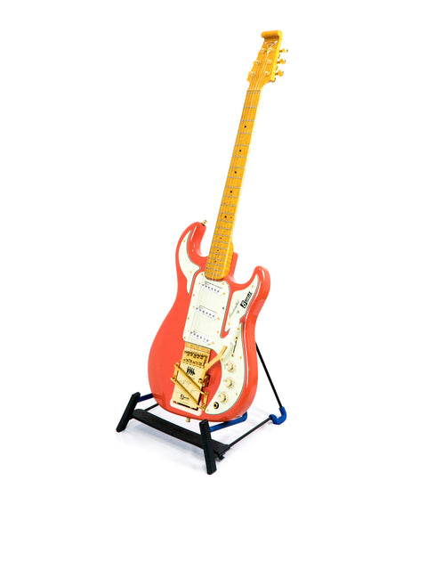 Red electric guitar with gold hardware on a stand against a white background.