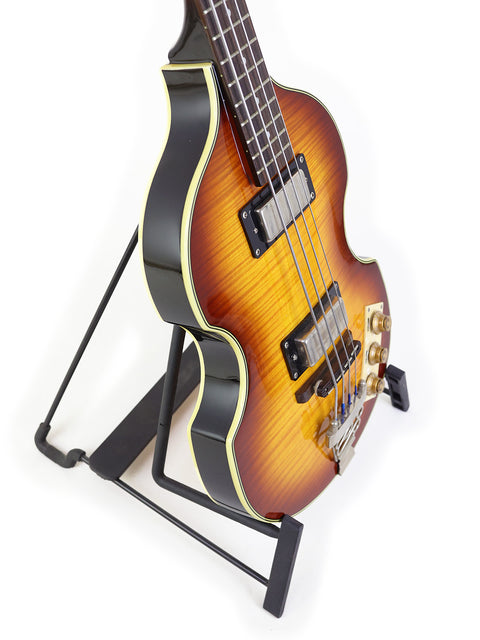 Sunburst electric bass guitar on a black stand against a white background.