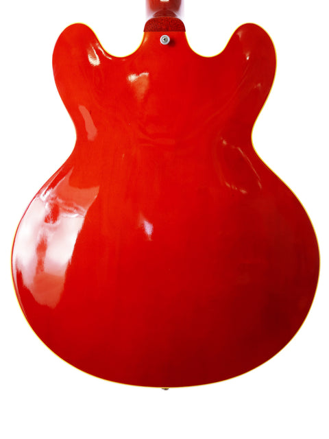 vibrant red Gibson ES-335 Block guitar displayed on a white backdrop, emphasizing its iconic shape and rich history.
