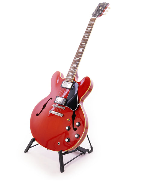 vibrant red Gibson ES-335 Block guitar rests on a stand, highlighted by a simple white background.